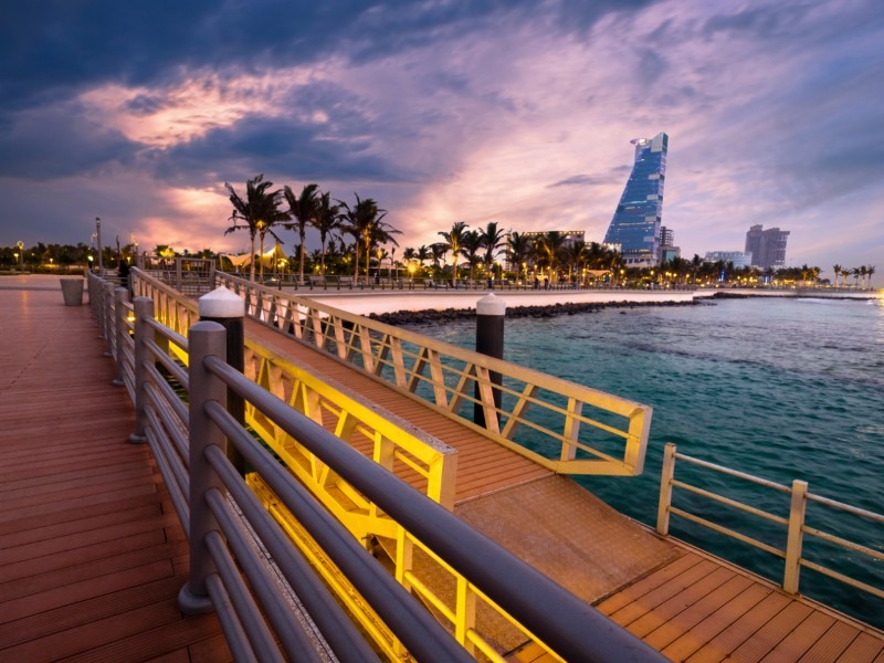 A pedestrian bridge and the Jeddah coastline at evening light